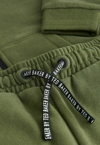 Olivno zeleni hlače s rebrastim manžetama, ki imajo vrvico z napisom "BAKER BY TED BAKER" in mehko teksturo.