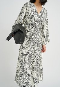 Lång, flödande klänning i svart och vitt med ett fjärilsmönster. Har en V-ringning och breda ärmar. Åtföljs av en svart kuvertväska.