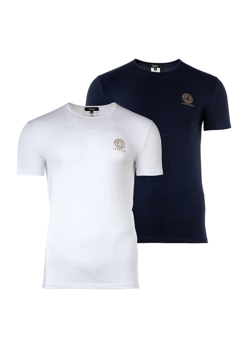 Dos camisetas de manga corta: una blanca y la otra azul marino. Ambas cuentan con un cuello redondo y un pequeño logo dorado en el pecho. Material de algodón, textura suave.