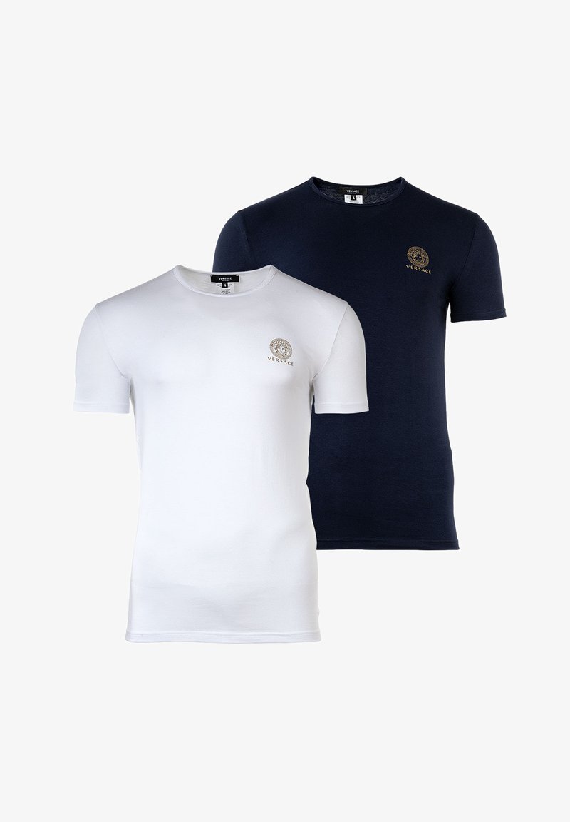 Dos camisetas de manga corta: una blanca y la otra azul marino. Ambas cuentan con un cuello redondo y un pequeño logo dorado en el pecho. Material de algodón, textura suave.