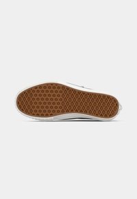 Suela de zapatilla de goma con un patrón texturizado en marrón, murallas laterales blancas y una parte superior negra contrastante. Presenta un diseño de banda de rodadura en forma de diamante.