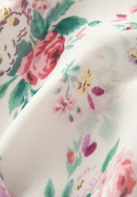 Weißer Stoff mit einem floralen Muster in Pink, Rot, Gelb und Grün. Weiche Textur mit verblassen Konturen von Blumen und Blättern in verschiedenen Größen.