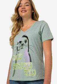 Camiseta de cuello en V verde claro con un gráfico de una foca y el texto "GOD STRAND TID" en colores contrastantes y en negrita. Tejido suave, mangas cortas.