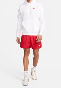 Vit huvtröja med rött Nike-logotyp, kombinerad med röda shorts med en liten vit Nike-logotyp. Bärs med vita och grå sneakers.