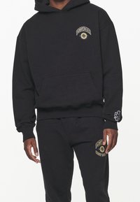 Felpa nera con cappuccio e tasca a marsupio, logo giallo ricamato sul petto, polsini a coste e pantaloni abbinati con dettagli simili al logo.