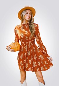 Vestido color óxido con patrones florales, mangas largas, cintura fruncida y falda acampanada. Combinado con un sombrero beige y sosteniendo una calabaza.