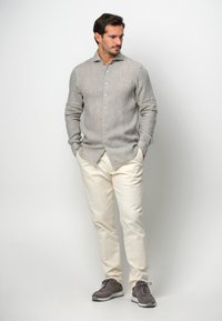 Camicia di lino grigio chiaro con bottoni e colletto, abbinata a pantaloni beige a gamba dritta e scarpe sportive grigie.