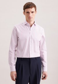 Camicia a righe in rosa chiaro e bianco, con colletto button-down e maniche lunghe con polsini a righe a contrasto. Indossati pantaloni scuri.