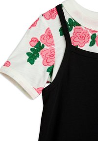 Chemise blanche à manches courtes avec motif de rose rose et feuilles vertes sous un haut noir sans manches à fines bretelles.