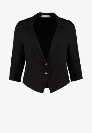 Blazer negro de manga tres cuartos, blusa crema, falda gris texturizada, media negras y botas de tobillo. Sostiene un clutch negro y plateado.