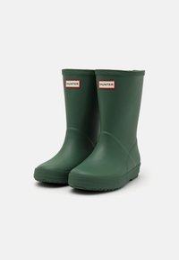 Stivali da pioggia in gomma verde con punta arrotondata, suola strutturata e etichette con logo sui lati. Finitura liscia e altezza a metà polpaccio.