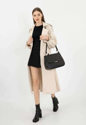 Cappotto trench beige con cintura, vestito nero aderente, stivali alla caviglia in pelle nera e borsa nera strutturata con manico superiore.