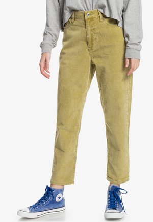 Khaki corduroy trousers with vertical ribbed texture, high waist, and straight legs, paired with blue denim sneakers.