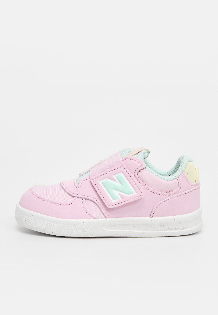 Baskets roses avec tige synthétique, lanière velcro, accents vert menthe clair, semelle blanche et bout arrondi. Présente un logo "N" surélevé sur le côté.
