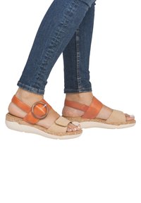 Des sandales bicolores avec un design en cuir tan et orange, une boucle circulaire surdimensionnée, et une semelle texturée et à motifs.