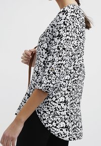 Svart och vit blus med ett strukturerat splattermönster, trekvartslånga ärmar, rundad nederkant och lös passform, bärs med axelrem.