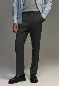 Pantalones gris ajustados de tela texturizada, con corte recto y bolsillos laterales, combinados con zapatos negros y una camisa rayada.