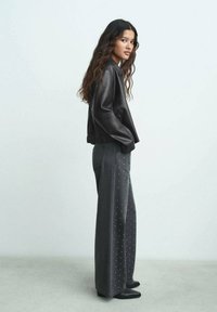 Giacca bomber in pelle nera con vita aderente, abbinata a jeans grigi scuri a gamba larga con dettagli in metallo argentato. Stivali completano l'outfit.