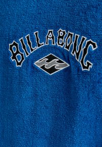 Blå frotté-stof med et broderet "Billabong" logo i sort over et diamantformet grafisk design med en stiliseret bølge i grå.