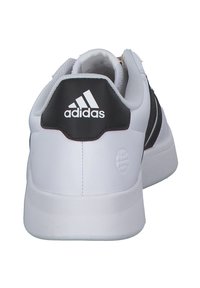 Vita idrottsskor med en slät läderöverdel, svart bakAccent och tre svarta ränder på sidorna. Har en texturerad sula.