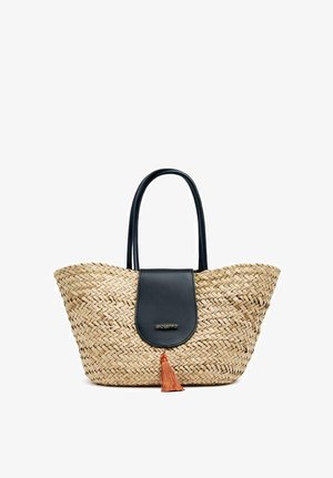 Bolsa de paja tejida con solapa de cuero negro y borla naranja. Forma redondeada, dos asas largas, superficie texturizada y acentos en contraste.