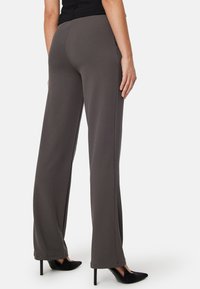 Pantalons larges gris en tissu lisse, dotés d'une taille haute et de coutures latérales. Complétés par des escarpins noirs à bout pointu.