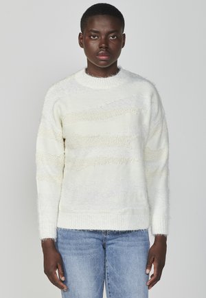 Maglione bianco con strisce testurizzate, realizzato in materiale morbido. Presenta un collo e polsini a costine, con una vestibilità comoda. Indossato con jeans blu.