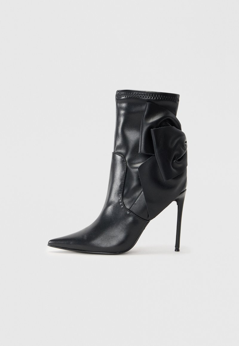 Black leather ankle boot with pointed toe, high stiletto heel, gathered fabric detail, and oversized black floral accent on the side.