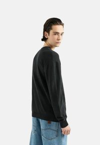 Maglione nero a maglia con maniche lunghe, design semplice e collo a giro. Indossato con jeans larghi di colore blu chiaro, che mostrano una vestibilità rilassata.