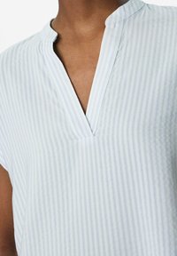 Lichtblauwe blouse met verticale witte strepen, een V-vormige halslijn en korte mouwen, gemaakt van een zachte, ademende stof.