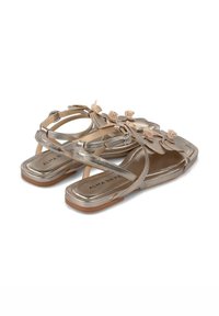 Metallisch gouden sandalen met bloemenversieringen en kruisbanden. Platte zool met een gladde textuur en een rechthoekige vorm. Merkenlabel zichtbaar.