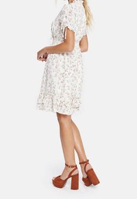 Vit blomstrig klänning med korta puffärmar, rynkade detaljer, volangkant, ihopparad med bruna mocka plattformsskor med ankelband.