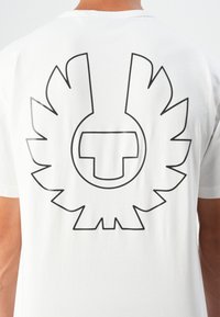 Person wearing white t-shirt featuring large black outlined bird with spread wings design on the upper back.