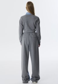 Grijze sweatshirt en wijde broek, gemaakt van zachte, gestructureerde stof. Heeft een denim kraag en een elastische tailleband met achterzakken.
