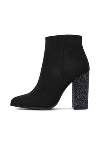 Stivale alla caviglia in suede nero con punta affusolata e tacco a blocco chunky coperto di glitter su uno sfondo bianco.