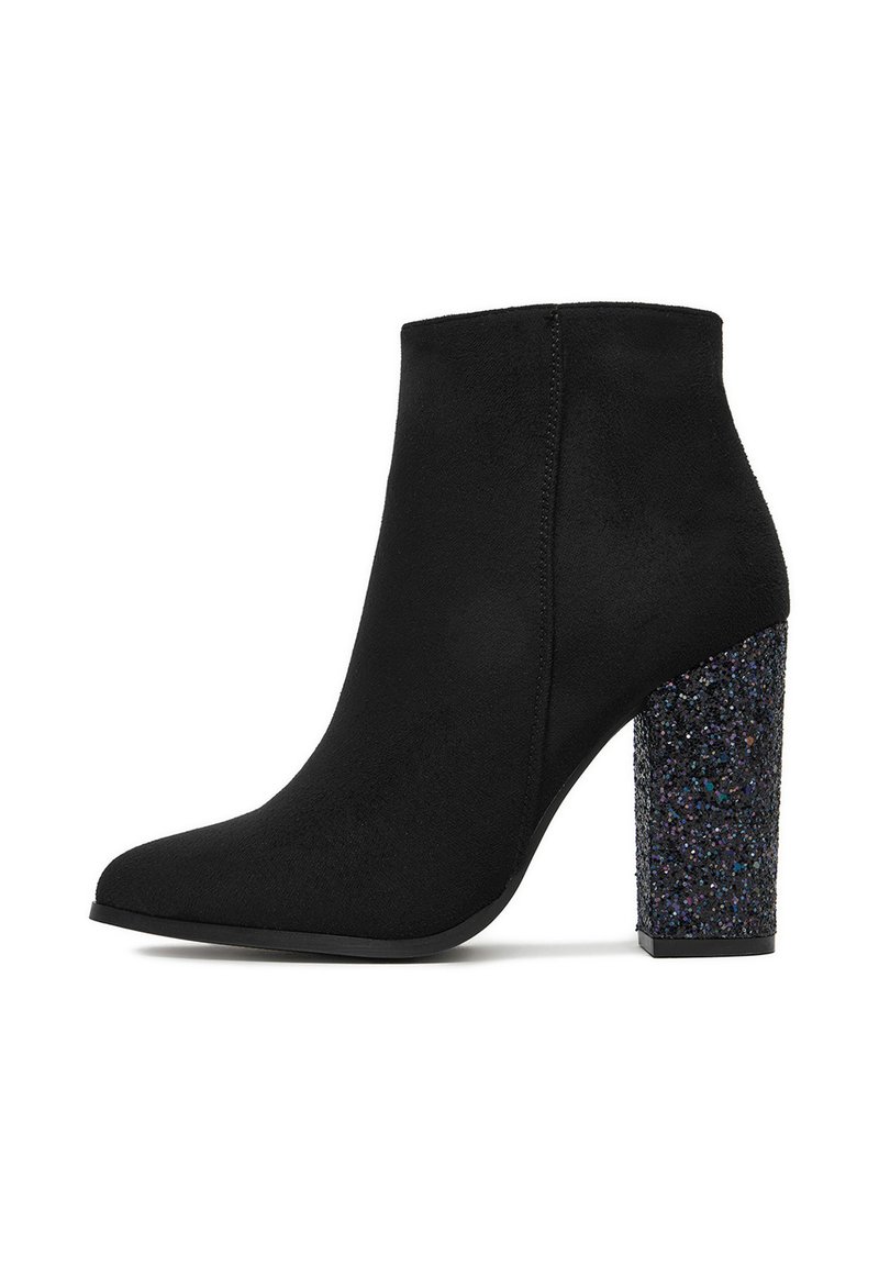 Stivale alla caviglia in suede nero con punta affusolata e tacco a blocco chunky coperto di glitter su uno sfondo bianco.