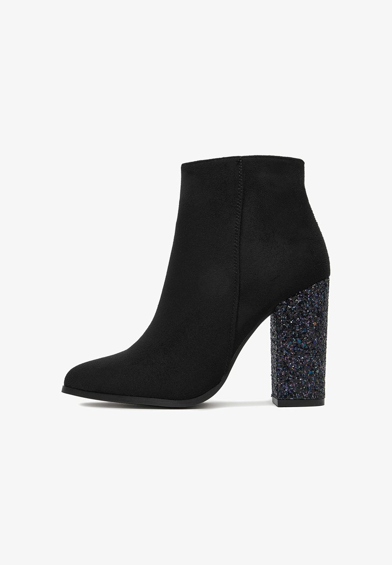 Stivale alla caviglia in suede nero con punta affusolata e tacco a blocco chunky coperto di glitter su uno sfondo bianco.