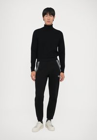 Suéter preto de gola alta combinado com calças de moletom pretas com riscas laterais e logótipo; ténis brancos completam o look.