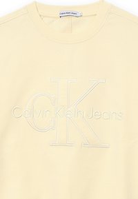 Felpa giallo chiaro con collo rotondo, caratterizzata da un logo ricamato "Calvin Klein Jeans" e un grande "CK" in filo bianco.