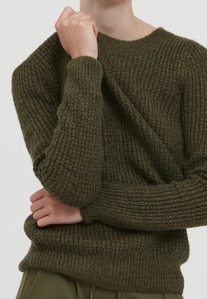 Pull en maille vert olive avec un motif texturé, encolure ronde et poignets côtelés. Le gros plan montre l'épaisseur et l'élasticité du tissu.