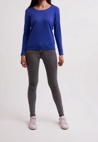 Blauw langemouwen shirt met een ronde hals, gecombineerd met grijze skinny jeans en witte sneakers. Geverst weefsel met een gladde afwerking.