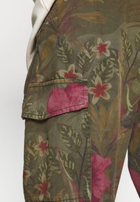 Olijfgroene cargoshorts van stof met roze en witte bloemenpatronen, een grote zijzak en een gestructureerde afwerking.