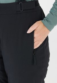 Zwarte softshellbroeken hebben een ritszak en een riemsluiting, gemaakt van rekbaar materiaal voor comfort en duurzaamheid.