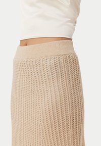 Stickad kjol i en ljus beige färg med ribbat mönster och ett mjukt, elastiskt midjeband. Har en figurnära silhuett och sömlös design.