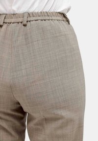 Graue, strukturierte Hose mit einem elastischen Bund und Gürtelschlaufen, versehen mit einem dezenten Muster aus helleren und dunkleren Fäden.
