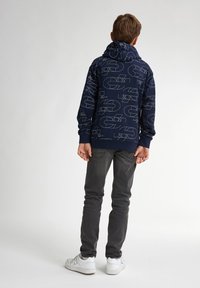 Sudadera navy con patrón geométrico blanco, diseño ajustado y capucha con cordón. Se lleva con jeans grises y zapatillas blancas.