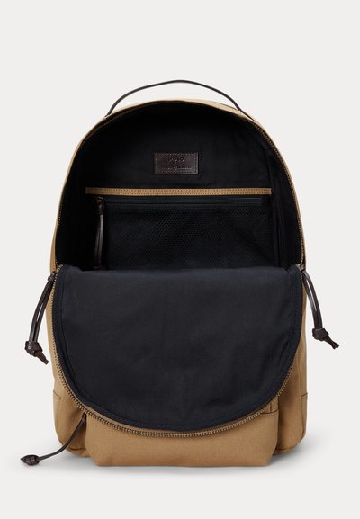 Hnedý batoh otvorený na zobrazenie čierneho interiéru s vreckom na zips z priedušnej sieťoviny a koženým rukoväťou.