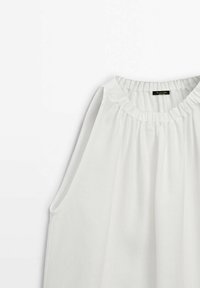 Blouse sans manches blanche en tissu léger, avec un col froncé et un drapé doux. Pas de boutons ni d'ornements supplémentaires.