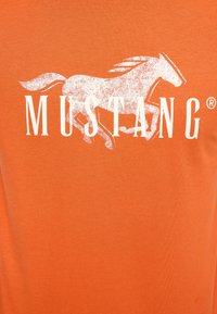 Orange t-shirt featuring a white graphic of a running horse and the text "MUSTANG" in bold capital letters. Soft, smooth fabric texture.