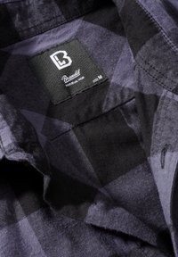 Zwarte en paarse geruite flanellen shirt met een label waarop 'Brandit', 'Individual Wear' en maat 'M' staat. Zachte stof met een gestructureerde afwerking.